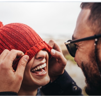 A man and woman joyfully laugh together both wearing bright red hats