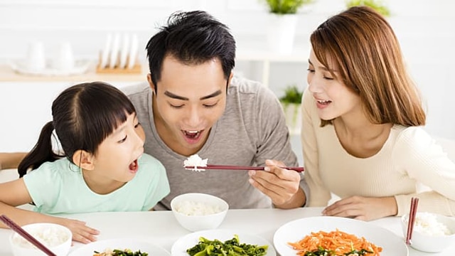 一家三口在餐桌前用筷子用餐微笑