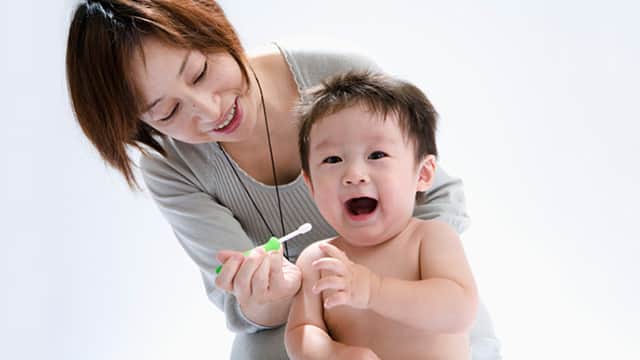 成人抱幼兒，用牙刷清潔牙齒