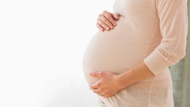 雙手托著孕肚，穿淺色上衣