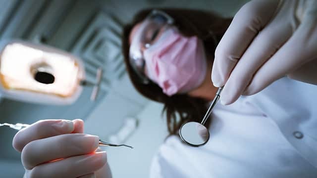 牙醫在診療燈下持口腔鏡與探針